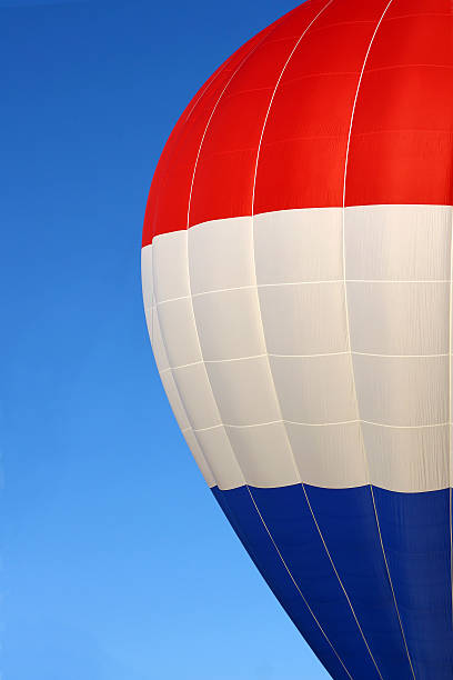 a close up on half of the side of a red, white, and blue hot air balloon, flying in front of a bright blue summer sky background