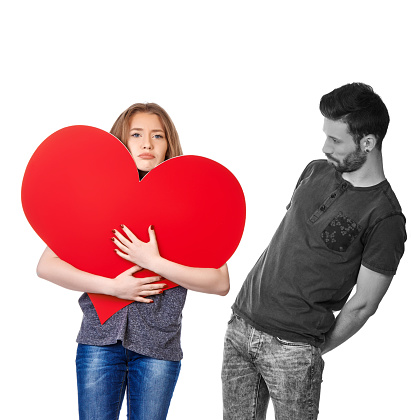 funny sad teenager girl embracing heartshape with empty space for text on it, man in black and white near her looking confused, white background.relationship difficulties concept.