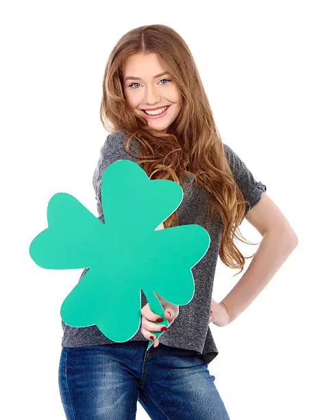 woman portrait with arms akimbo holding green four leafs clover and smiling, white background. St.Patrick's day celebration.