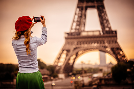 Photo of stylish woman photographing the Eiffel Tower with smartphone