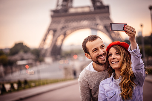 Photo of happy smiling couple making selfie in front of the Eiffel Tower in Paris, France