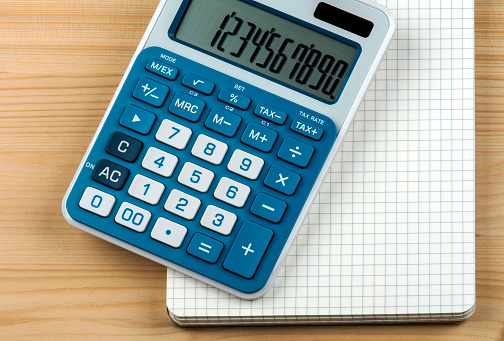 Close-up of blue and white calculator with notepad on wooden background.