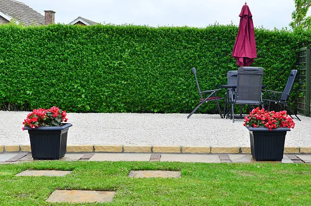 A Gravel patio area with table chairs and parasol with two planters, outside dining area.