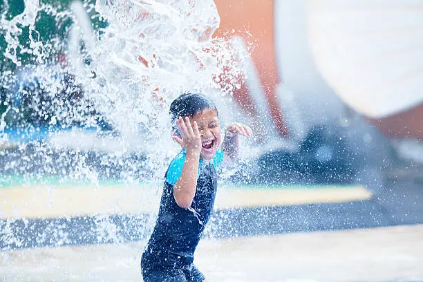 Asian boy having fun with pool fountain shot duing summer time