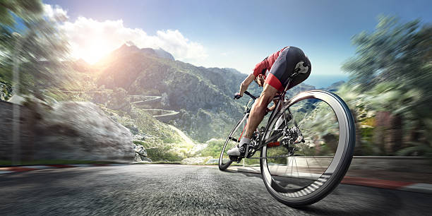 Professional road cyclist An athlete is riding a bicycle on a spiral track high in the mountains.  The man is wearing black bike shorts and shin guards along with a red sleeveless top and a red and white helmet and sunglasses. The image is blurred in motion. racing bicycle photos stock pictures, royalty-free photos & images