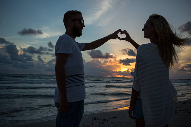 istock Silhouette of couple on beach making heart shape 476279384