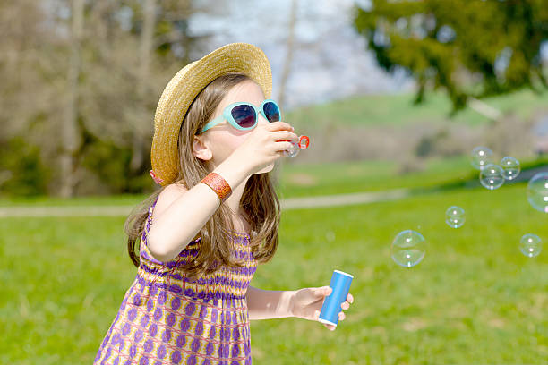 a little girl making soap bubbles with sunglasses in nature