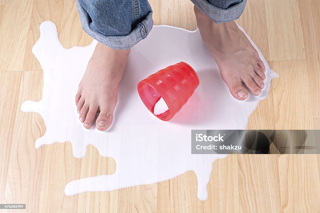 Spilled milk Child's bare feet standing in puddle of spilled milk on wood floor with red cup Child Stock Photo