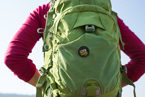 Rear view close up of a woman wearing a colorful backpack.She has a small text badge with Live Loud inscription