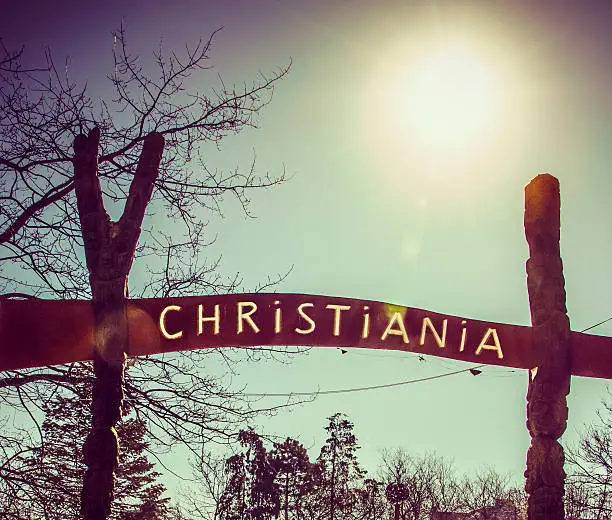 Under a bright sun, a sign with the name of Christiania,  at one of the entrances of this self-proclaimed autonomous town, inside the city of Copenhagen. 