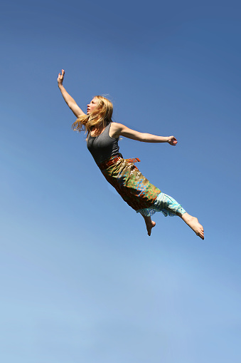 A young woman is jumping up as if flying through the air in front of a blue sky background.