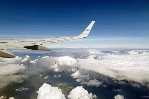 Wing Tip of KLM Aeroplane over Cumulus Clouds and Land with Blue Skies and Copy Space 