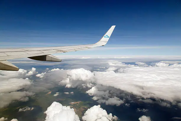 Wing Tip of KLM Aeroplane over Cumulus Clouds and Land with Blue Skies and Copy Space 