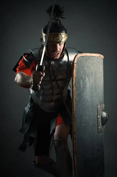 Roman legionary with sword and shield in the attack isolated on gray background