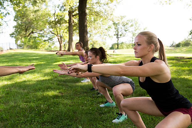 Group of People Exercising in the Park A group of four women  exercise together outdoors in a park.  The group are doing a boot camp style workout.  They are in the grass doing squats.  Springtime, lots of green in the composition.  Shot in Atlanta, Georgia. fitness boot camp stock pictures, royalty-free photos & images