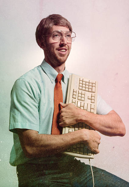 Eighties Computer Genius Portrait A nerd computer tech guy poses for a glamour portrait hugging his computer keyboard with love. Vintage 1980's emulation and style of the portrait and the clothing and technology. A funny and humorous depiction of the digital technology of decades past. nerd stock pictures, royalty-free photos & images