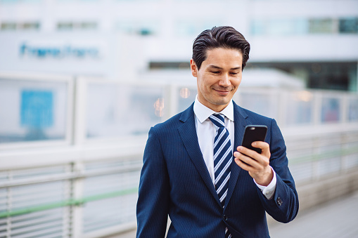 Young businessman with suit using smart phone at urban scene