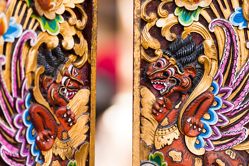 This is a horizontal, color, royalty free stock photograph of beautifully carved wooden doors in Ubud, a travel destination on the exotic tropical island of Bali in Indonesia. Traditional symbolic Hindu figures are ornately painted all over the Southeast Asian city. Depth of field is shallow. Photographed with a Nikon D800 DSLR camera.