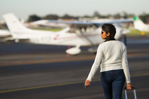 A tourist walking towards a small aircraft pulling her suitcase.