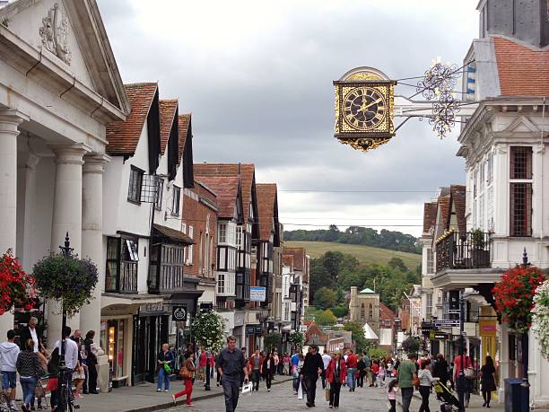 Guildford High Street on a summer's day Guildford is a picturesque market and university town in Surrey. this photo shows the town hall clock and the steep slope of the high street going towards the River Wey. surrey england stock pictures, royalty-free photos & images