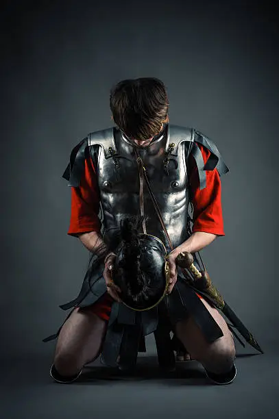 man kneeling with a helmet in hands isolated on gray background