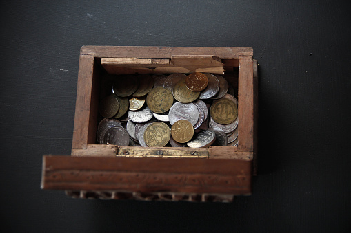 Antique treasure chest full of silver and golden coin. The photo shot on studio on black background. Treasure chest containing buried currencies are part of the popular beliefs surrounding pirates and out laws. 