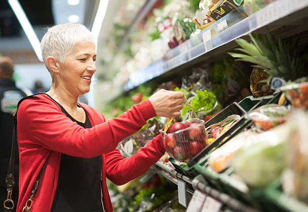 Mature woman shopping at market Mature woman shopping at supermarket produce section stock pictures, royalty-free photos & images