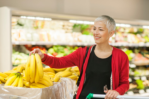Mature woman shopping at supermarket buying bananas