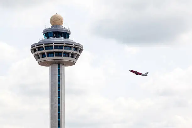 Singapore Changi International Airport traffic controller tower with airplane taking off in the background. The unique airport tower is one of the most recognizable icons of Singapore.