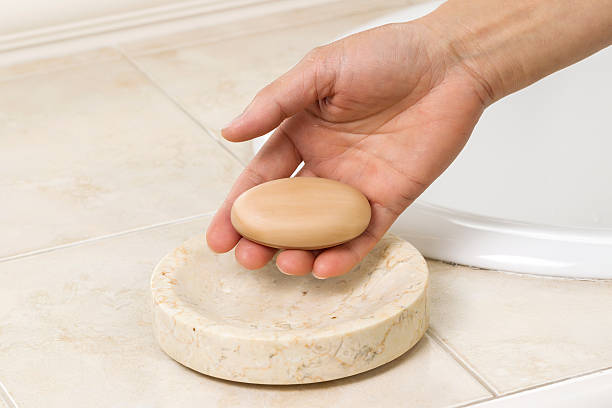 Horizontal photo of female hand holding bar of soap with bathroom sink in background