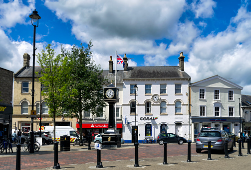 Stowmarket, Suffolk, England - May 12, 2015: Two clocks - both showing different times - in the Market Place in Stowmarket, Suffolk, England. Stowmarket is a typical small English town with a variety of shops. (Background people.)