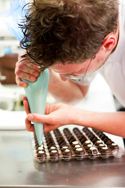 istock Chef pipes cream into chocolate moulds before making truffles 476383615