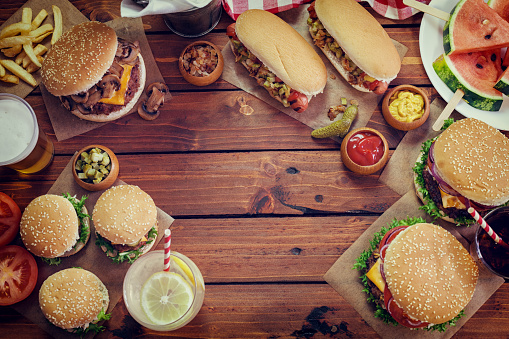 Food served at a picnic table for July 4th.On the table are traditionally grilled dishes American hamburgers and hot dogs, beer, lemonade, cola and watermelon.