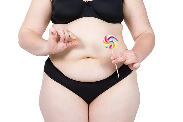 Woman showing her fat body and holding a lollipop and tablets. Healthy lifestyles concept and diet.