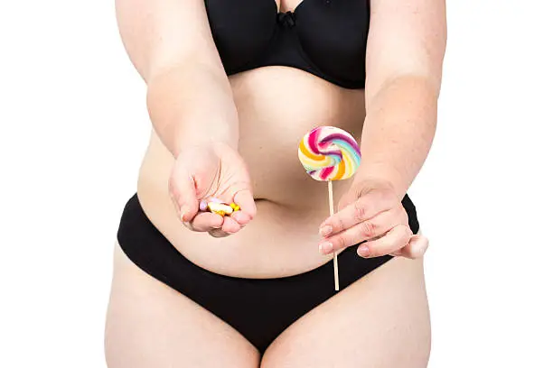 Woman showing her fat body and holding a lollipop and tablets. Healthy lifestyles concept and diet.