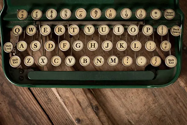 Close up, color image of a vintage, green, manual typewriter's keys, sitting on wood trunk.