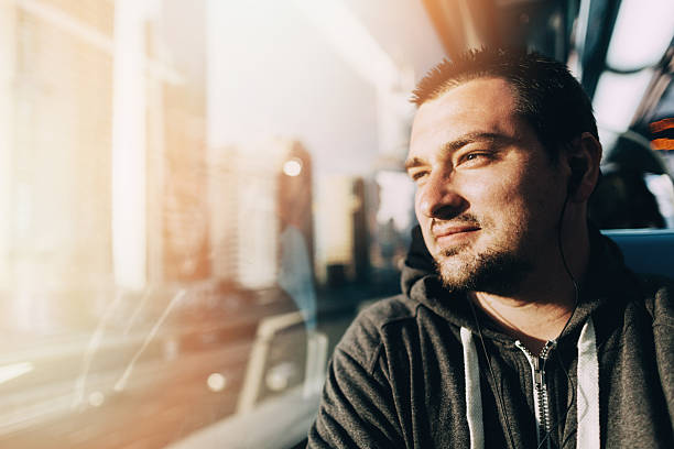 Young man is traveling in the train. He is looking through the window and smiling. There is modern panorama of the city and he is admiring it.