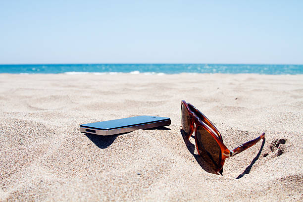 Smartphone and sunglasses on the beach with the blue sea in background 
