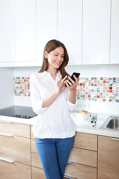 istock Young woman using cell phone in the kitchen 476418258