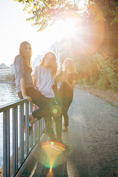 female friends sit and lean against a railing, on urban background, back lit