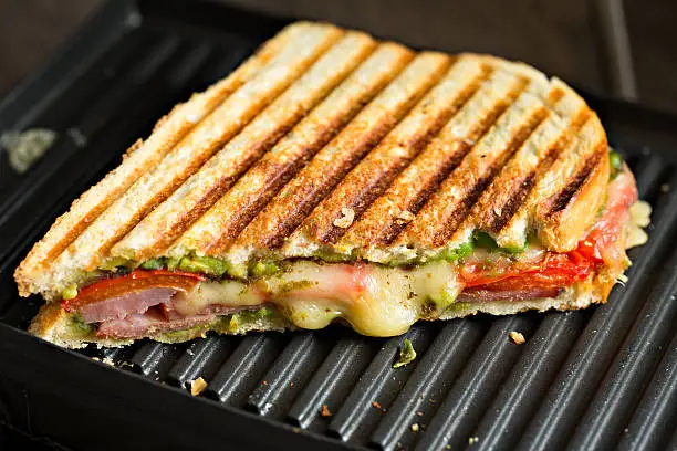 A high angle extreme close up shot of half a ham and cheese panini on a panini maker grill.