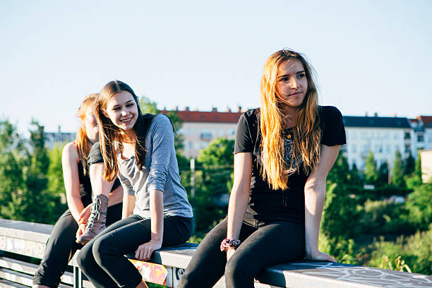 small group of young women sitting together on a railing on urban background in summer