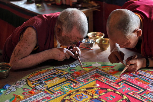 Ladakh, Jammu & Kashmir, India - September 3, 2011: Buddhist monks making sand mandala in Diskit gompa (monastery) at Nubra Valley. This is a Tibetan tradition of creation and destruction of mandala made from colored sand. Mandala - is a spiritual and ritual symbol in Hinduism and Buddhism, representing the Universe.