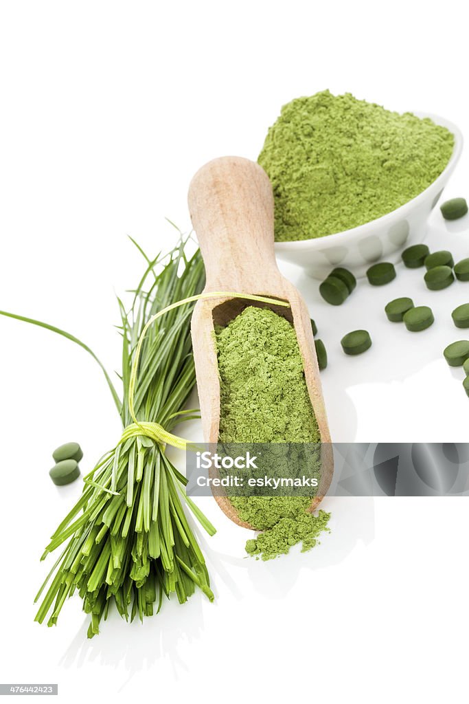 Wheatgrass powder and pills. Superfood. Natural herbal organic alternative medicine. Superfood. Wheatgrass powder, blades and green pills on wooden scoop and white bowl isolated on white. Healthy lifestyle. Ground - Culinary Stock Photo