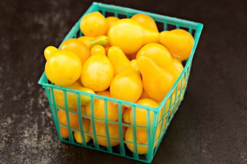 A high angle close up shot of a plastic basket full of Locally grown organic yellow pear cherry tomatoes.