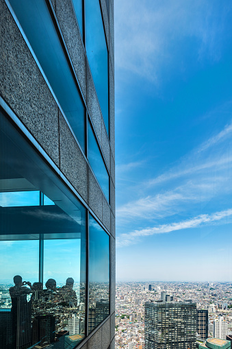 Silhouettes of people in Tokyo looking at the city from an office tower. The vast city and the blue dramatic sky is reflected in the window