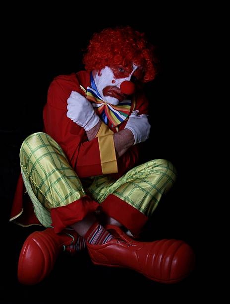 traurig clown auf dem boden sitzen und gekreuzte beine - clown mime sadness depression stock-fotos und bilder