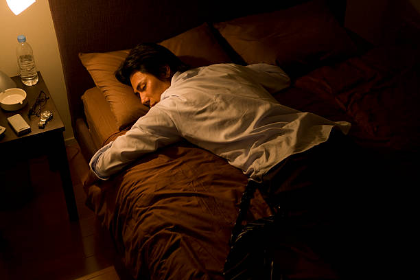homme d'affaires dormir sur le lit avec costume usé - être étendu sur le ventre photos et images de collection