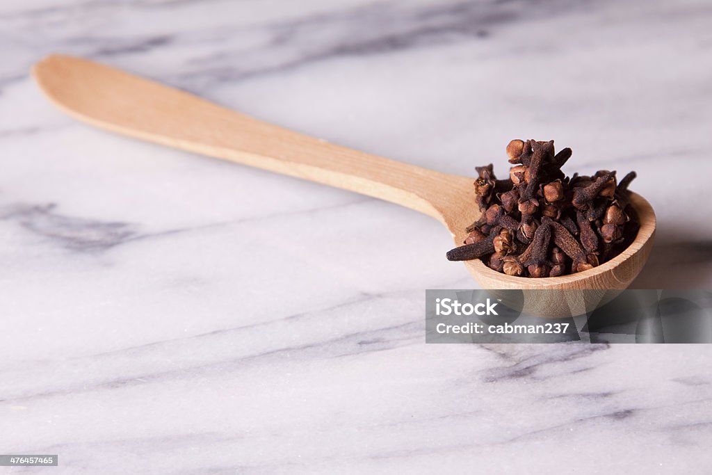 Cloves A wooden spoon full of cloves on a marble background Close-up Stock Photo