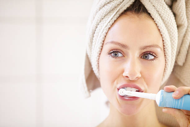 Keeping her teeth in great shape - Dental hygiene Young woman brushing her teeth with an electric toothbrush woman wrapped in bath towel stock pictures, royalty-free photos & images
